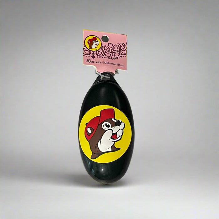 Buc-ee’s detangler brushes in two colors: one black with Buc-ee in a red cap, and one purple with Buc-ee surrounded by pink hearts, shown from front and back views.