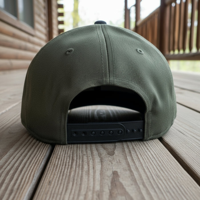 Back view of an olive-green and black Buc-ee’s hat showing the adjustable snapback closure, displayed on a cabin porch.