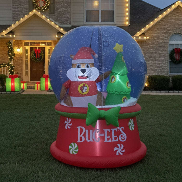 Inflatable Buc-ee’s Christmas snow globe featuring Buc-ee the Beaver dressed in a Santa outfit standing beside a decorated Christmas tree with a star on top, on a red base with “Buc-ee’s” written on it, displayed outdoors on a lawn.