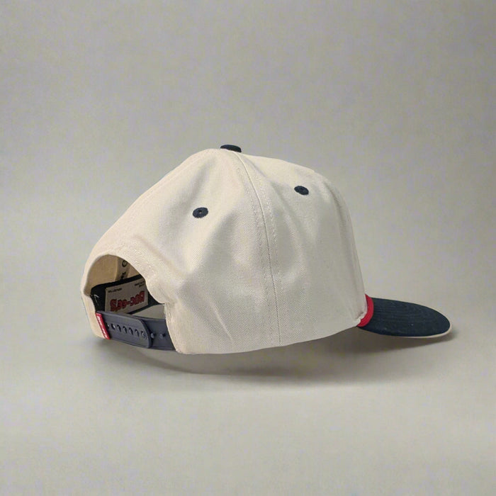 Side view of Buc-ee’s "Fresh Brisket on the Board" snapback hat on white table, showing cream crown and navy bill