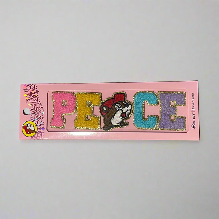 Two Buc-ee’s sticker patches shown on pink packaging: one spells “LOVE” with Buc-ee’s face as the “O,” and the other spells “PEACE” with Buc-ee in the center, both in colorful glitter letters.