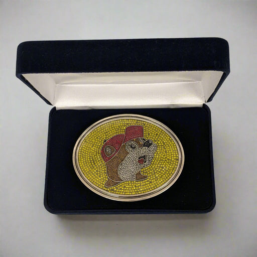 "Limited Edition Buc-ee's Rhinestone Belt Buckle in a black velvet display box, featuring the iconic beaver logo with sparkling rhinestones on a yellow background and red cap detail."