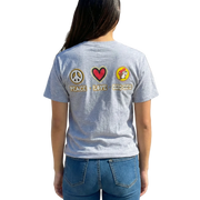 Person wearing a gray t-shirt with peace, love, and friendship patches in front of a gas station.