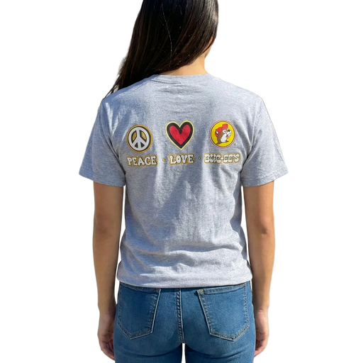 Person wearing a gray t-shirt with peace, love, and friendship patches in front of a gas station.