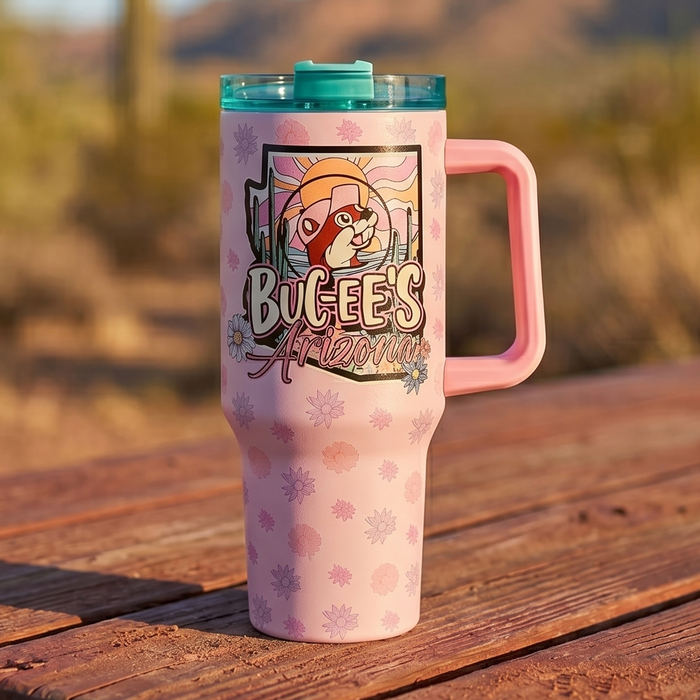 Pink tumbler with 'Bucees' logo on a wooden table in a desert setting