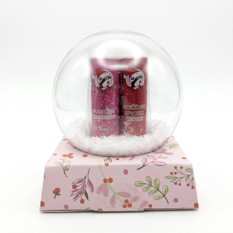 Buc-ee's snow globe lip balm gift set showing Sugared Cranberry and Holiday Spiced Cider lip balm tubes sitting in white faux snow.