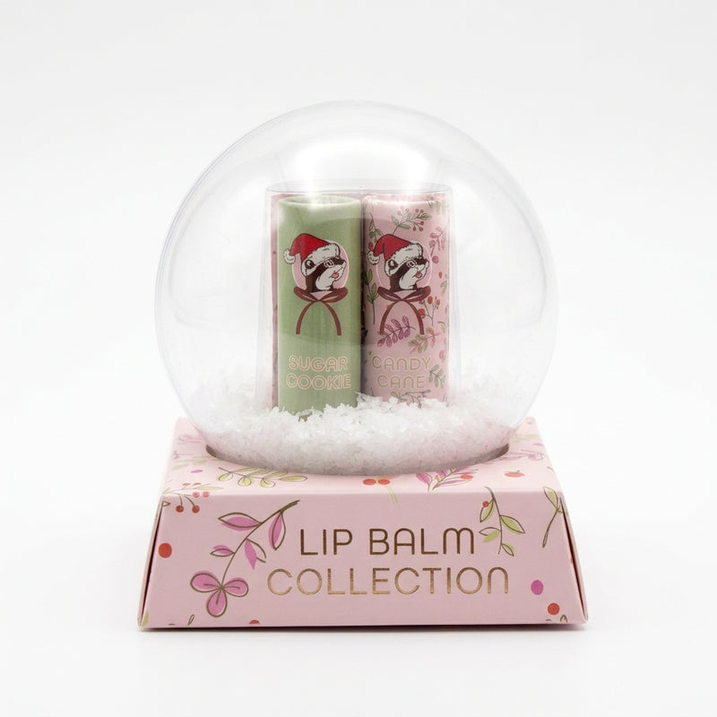 Buc-ee's Lip Balm Collection packaging styled like a clear snow globe on a pink floral base displaying "LIP BALM COLLECTION" with Sugar Cookie and Candy Cane lip balms inside.