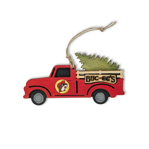 Buc-ee's wooden Christmas ornament shaped like a vintage red pickup truck hauling an evergreen tree with the Buc-ee's logo on the door and a twine hanging loop.