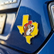 A close-up shot of the Buc-ee’s Texas Chrome Emblem affixed to the rear bumper area of a navy blue car, showing the bright yellow state outline, chrome border, and smiling Buc-ee beaver mascot in crisp detail.