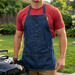 Man wearing a branded apron standing next to a barbecue grill in a backyard setting.