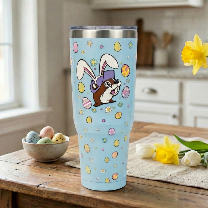 Blue tumbler with a cartoon dog in bunny ears on a wooden table with flowers and eggs.