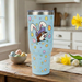 Blue tumbler with a cartoon dog in bunny ears on a wooden table with flowers and eggs.