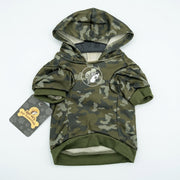 Front view of a green camo pet hoodie flat lay with an attached hood, olive green ribbed hem, a Buc-ee's chest logo, and a Buc-ee's Pet Essentials hangtag.