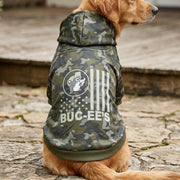 Back view of a golden retriever sitting outdoor on a stone patio while wearing the Buc-ee's green camo pet hoodie, highlighting the white US flag print and Buc-ee's beaver logo on the back.