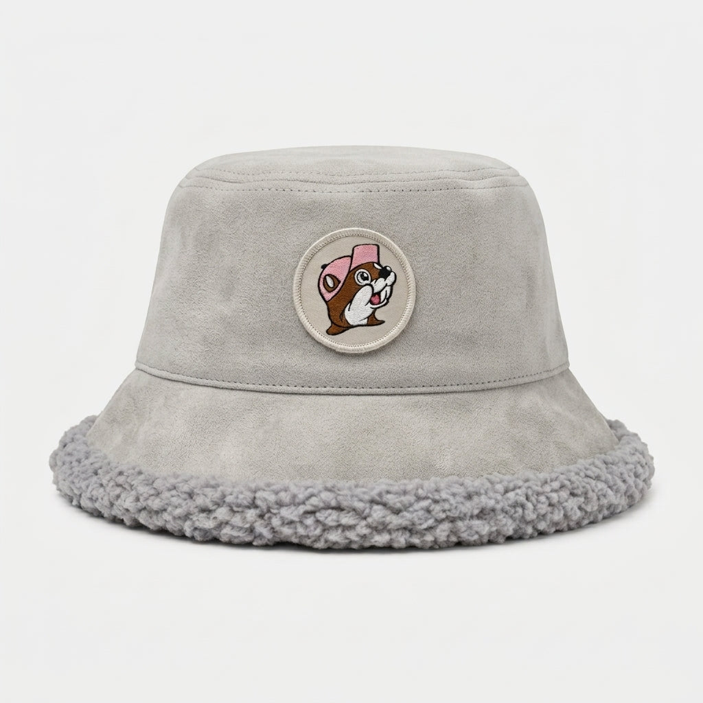 Buc-ee's light gray faux-suede bucket hat with a fuzzy light gray sherpa interior lining and brim trim, featuring a circular front patch of Buc-ee the Beaver wearing a pink cap.
