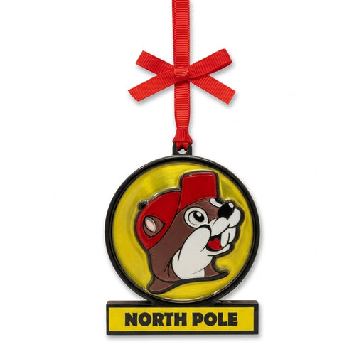 Buc-ee's metallic foil Christmas ornament designed like a yellow billboard sign with Buc-ee the Beaver, a "NORTH POLE" banner, and a red ribbon bow.