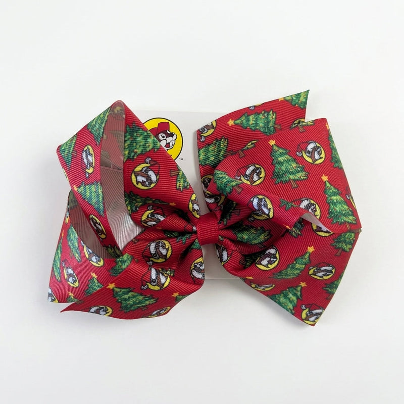Large red grosgrain hair bow printed with Santa Buc-ee logos and decorated Christmas trees, centered with a red ribbon knot on a display card.