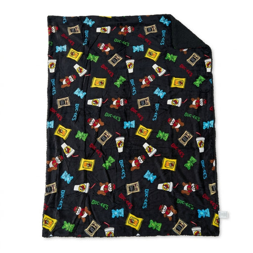 Black Buc-ee's sherpa-lined throw blanket laid flat, featuring a colorful print of Beaver Nuggets, drinks, gummy bears, beef jerky, and Buc-ee's logos.