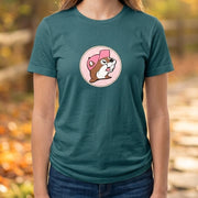 A woman standing on an autumn path wearing a teal t-shirt with a circular graphic of a cartoon chipmunk wearing a pink hat, paired with blue jeans.
