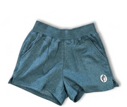A pair of heathered teal blue athletic shorts with a wide elastic waistband and side pockets, featuring a small circular logo patch on the lower left leg, shown against a plain white background.