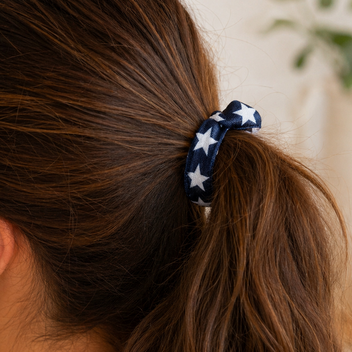 Close-up of a brunette woman’s ponytail secured with a navy blue hair tie featuring white star patterns, styled in a soft, natural indoor setting with warm lighting and minimal background distractions.
