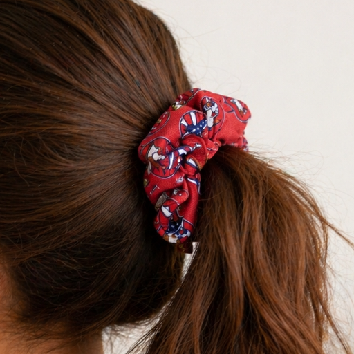 Red patterned scrunchie with patriotic Buc-ee’s beaver logos securing a brunette woman’s ponytail, shown in a soft, natural-light indoor setting with minimal background decor.