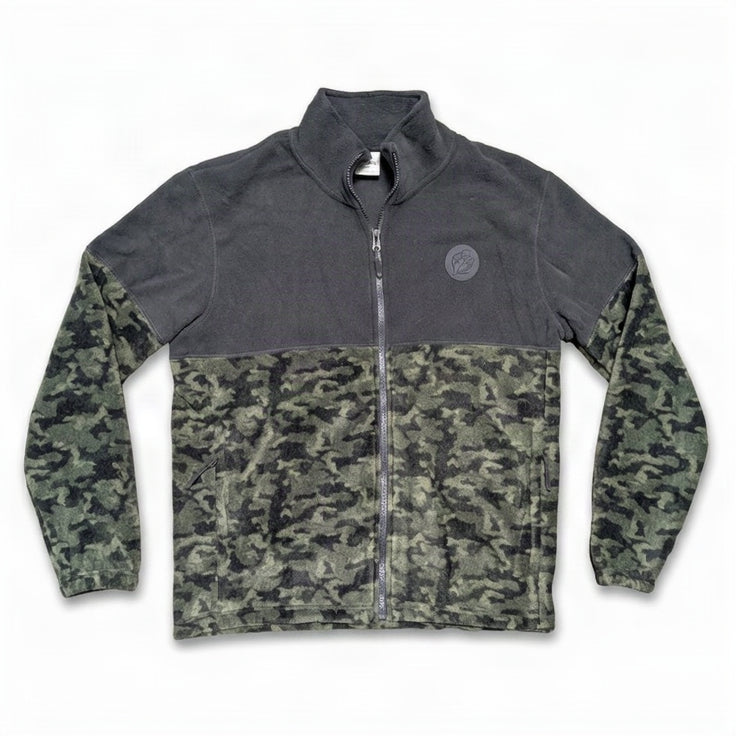 A front flat-view photo of a Buc-ee's men's full-zip fleece jacket on a white background. The jacket features a solid charcoal grey upper section, a dark camouflage lower body and sleeves, a round grey Buc-ee's beaver logo patch on the left chest, and side zippered pockets.