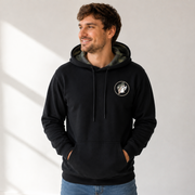 Man wearing a black Buc-ee’s hoodie with a camouflage-lined hood, drawstrings, circular beaver logo on the chest, and kangaroo pocket, paired with blue jeans.