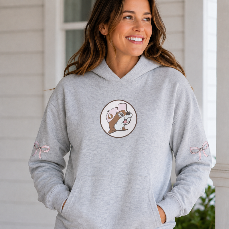 Woman wearing a gray logo bow Buc-ee’s hoodie with a Buc-ee beaver logo on the chest and pink bow designs on the sleeves.