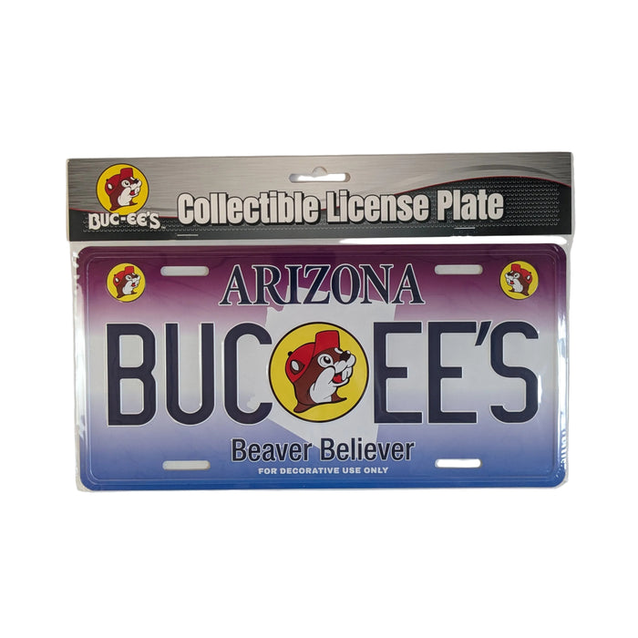 Official Buc-ee's Arizona Collectible License Plate in its clear plastic packaging. The metal plate features a purple-to-blue desert gradient background with a white silhouette of the state of Arizona, large white text spelling "BUC-EE'S", and the iconic beaver mascot in the center. Displayed on a clean white background.