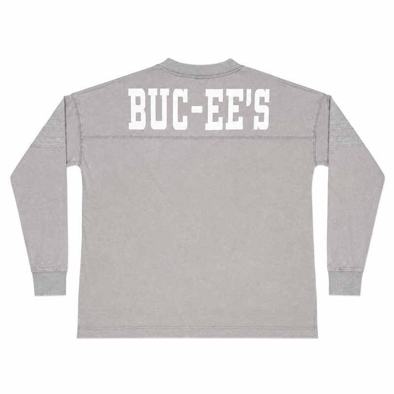 Back view of a mineral-washed ash grey long-sleeve tunic shirt featuring large white "BUC-EE'S" block letters across the back shoulders.