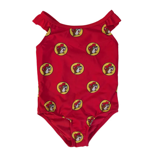 A flat lay product photograph of a Buc-ee's Baby Girl Red Logo one-piece swimsuit on a clean white background. The swimsuit features ruffle details on the shoulder straps and is covered in a dense, repeating pattern of the yellow and red Buc-ee’s beaver logo. 