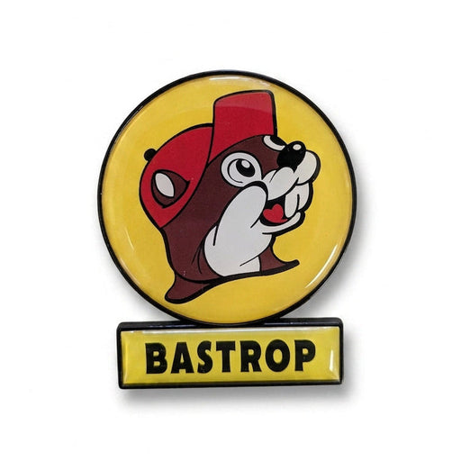 A circular yellow enamel magnet featuring the smiling Buc-ee's beaver wearing a red hat, with a small rectangular yellow sign attached directly below reading "BASTROP" in black text.