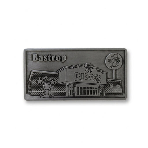 A rectangular antique pewter metal magnet with 3D relief detailing of the Buc-ee's Bastrop storefront. Features "Bastrop, TX" engraved in the upper left corner, the Buc-ee's store building with main entrance, the beaver mascot statue out front, and the tall roadside lollipop sign on the right.