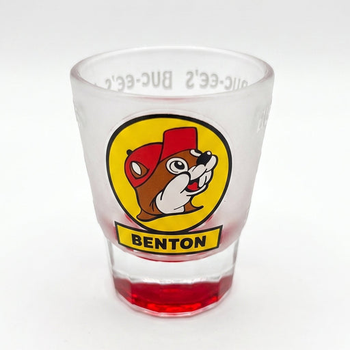 A clear glass shot glass featuring a circular yellow and red logo with a bulldog and the word 'BENTON' on the front, with a red tinted base, set against a plain white background.
