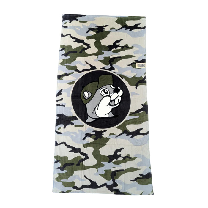 A rugged beach towel with a classic green and tan forest camouflage pattern. A large black circle in the center features the iconic Buc-ee's beaver mascot. Displayed on a clean white background.