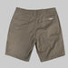 A back view of the Buc-ee's Caribou Fishing Twill Shorts in a deep earth-brown taupe, shown laid flat against a neutral grey background. The image highlights the clean, durable construction of the cotton-twill fabric, featuring two horizontal welted back pockets and reinforced belt loops. A small, white rectangular "Buc-ee's" logo patch is sewn above the right rear pocket. On the far right edge, the side-entry utility tool slot is partially visible.