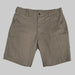 A front view of the Buc-ee's Caribou Fishing Twill Shorts in deep earth-brown taupe, shown laid flat against a neutral grey background. The image features a classic button-waist closure with a zipper fly, deep front slash pockets, and reinforced belt loops. On the right leg (viewer's left), a low-profile, horizontal-entry utility tool slot is visible, designed for quick access to gear. The heavy-duty cotton-twill fabric displays a rugged, matte texture suitable for outdoor use.