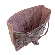 An angled, overhead view looking into the open main compartment of a Buc-ee's Cherry quilted tote bag. The interior features a fine pink-and-white vertical stripe lining and a built-in fabric slip pocket printed with cherries and the Buc-ee's beaver mascot. The outer side and matching striped shoulder straps are also visible against a white background.