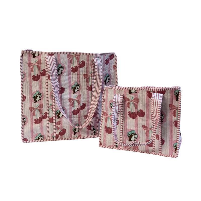 Two quilted tote bags—one large and one small—standing upright on a white surface. The bags feature a pink and white vertical stripe pattern printed with Buc-ee's beaver mascots, pink cherries, and bows, finished with matching striped shoulder straps.