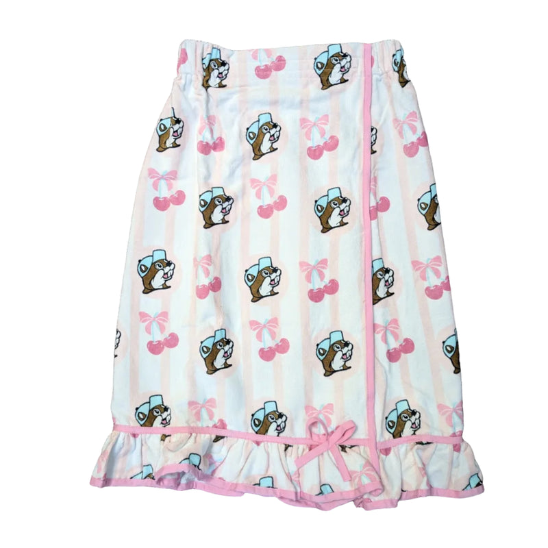 An overhead view of a Buc-ee's Cherry Towel Wrap, a vertically striped pink and white spa towel wrap with an allover print of the Buc-ee's beaver mascot, bows, and pink cherries. It features an adjustable Velcro and elastic closure at the top and a ruffled hem accented with a pink bow. Displayed on a white background.