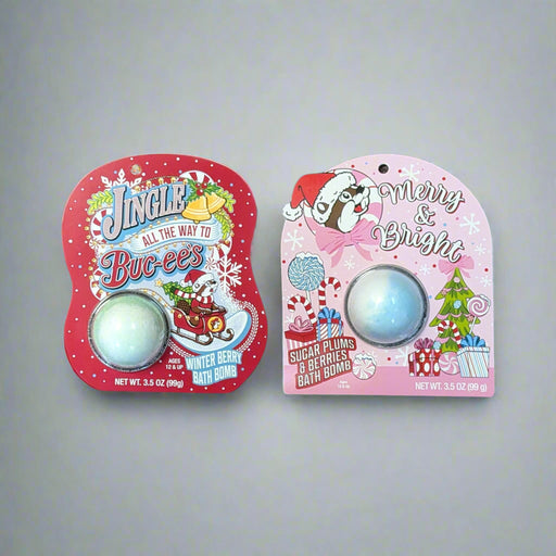 Two Buc-ee’s Christmas bath bombs — one in pink “Sugar Plum” packaging and one in red “Winter Berry” packaging — displayed on a carpet background.