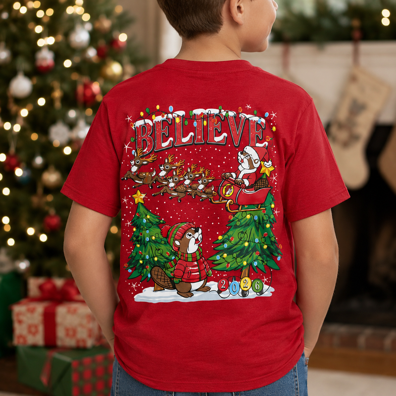 Youth wearing a red Buc-ee’s Christmas T-shirt featuring a colorful “BELIEVE” Santa and reindeer design, shown from the back in a festive Christmas setting.
