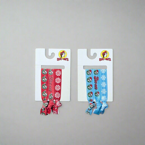 Two packs of Buc-ee’s Christmas Hair Ties – one blue Snowflake set and one red Peppermint set, each with Buc-ee holiday designs.