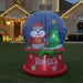 Inflatable Buc-ee’s Christmas snow globe featuring Buc-ee the Beaver dressed in a Santa outfit standing beside a decorated Christmas tree with a star on top, on a red base with “Buc-ee’s” written on it, displayed outdoors on a lawn.