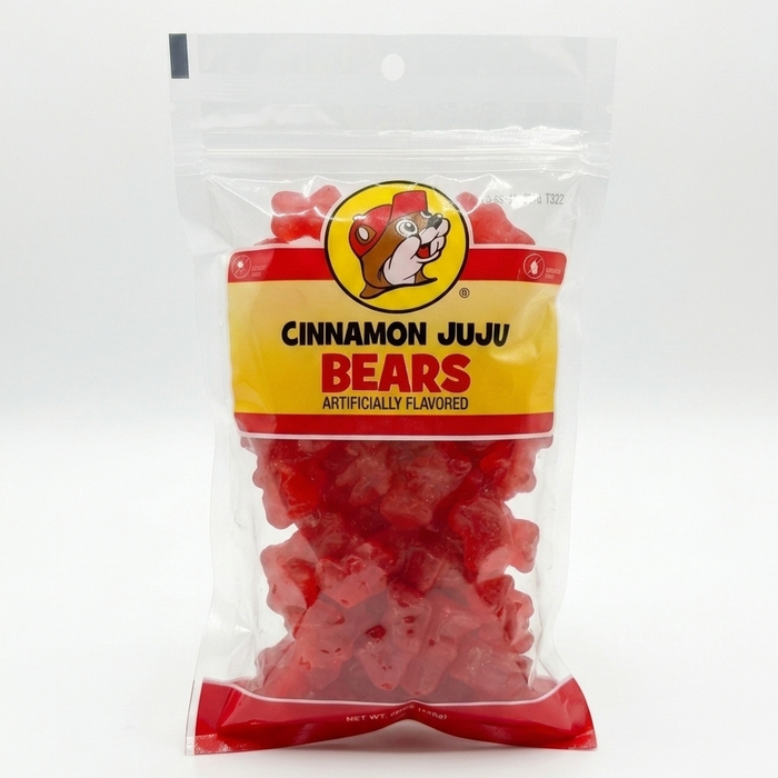 A product shot of a 12 oz bag of Buc-ee’s Cinnamon Juju Bears centered against a clean, solid white background. The clear resealable packaging prominently features the yellow Buc-ee’s beaver logo above bold black and red text reading "CINNAMON JUJU BEARS." Inside the bag, the large, thick, bright red bear-shaped candies are clearly visible. The lighting is bright and even, highlighting the glossy texture of both the packaging and the chewy candies.