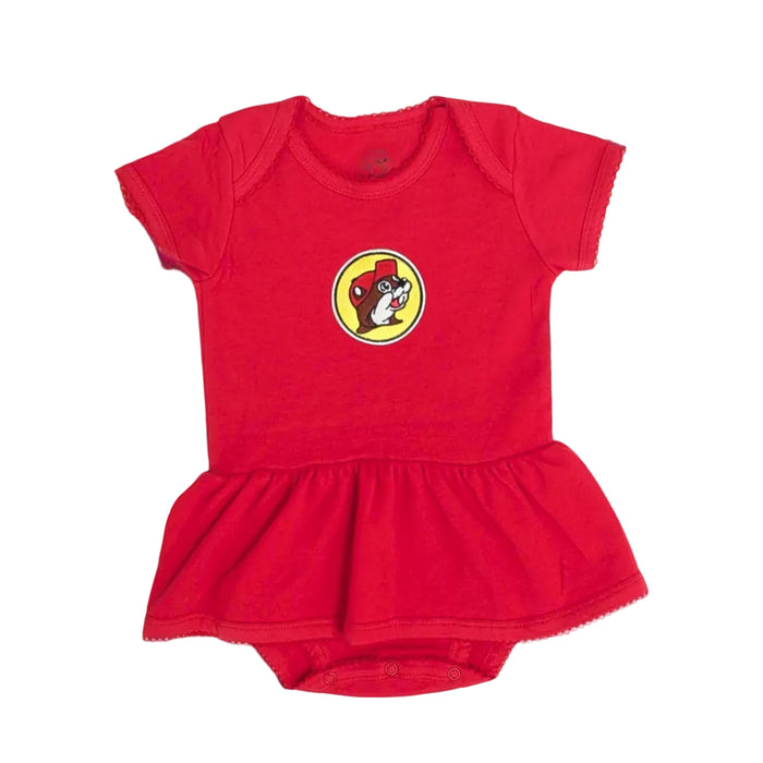 A flat-lay product photograph centered on a white background showing a vibrant red Buc-ee's infant onesie dress. The short-sleeve knit bodysuit features a yellow circular patch with the classic cartoon Buc-ee the Beaver logo on the chest. It includes a built-in ruffled skirt, a snap-button bottom closure, and delicate scalloped embroidery details running along all edges, including the neckline, sleeve cuffs, and skirt hem.