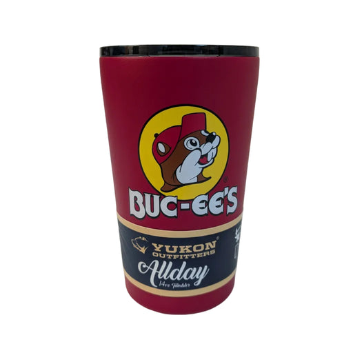 The Buc-ee's Classic Red All Day Tumbler, a 14oz matte red stainless steel cup featuring the yellow Buc-ee's beaver logo. It is topped with a translucent black smoke lid and shown with the removable navy "Allday" Yukon Outfitters packaging around the base. Displayed on a clean white background.