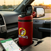 A lifestyle image of a classic red Buc-ee's Hydrobubble tumbler sitting in a vehicle's center console cup holder. The tumbler features the classic yellow and black circular Buc-ee's beaver mascot logo on the front. Its black and red flip-top lid is propped open, revealing a drinking spout. In the foreground, a smartphone lies flat on the console displaying a navigation map app. The background shows a vehicle interior with a side-view mirror, softly blurred against a warm sunset light.