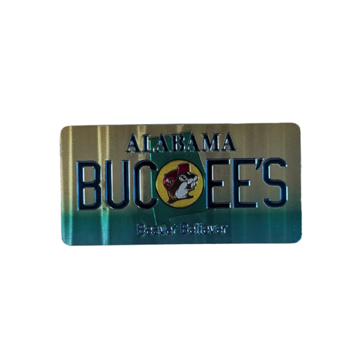One side of a rectangular metallic Buc-ee's Alabama Double-Sided souvenir magnet laid flat on a white surface. This side of the magnet features a gold-and-green gradient background with embossed text reading "ALABAMA BUC-EE'S" and "Beaver Believer." 